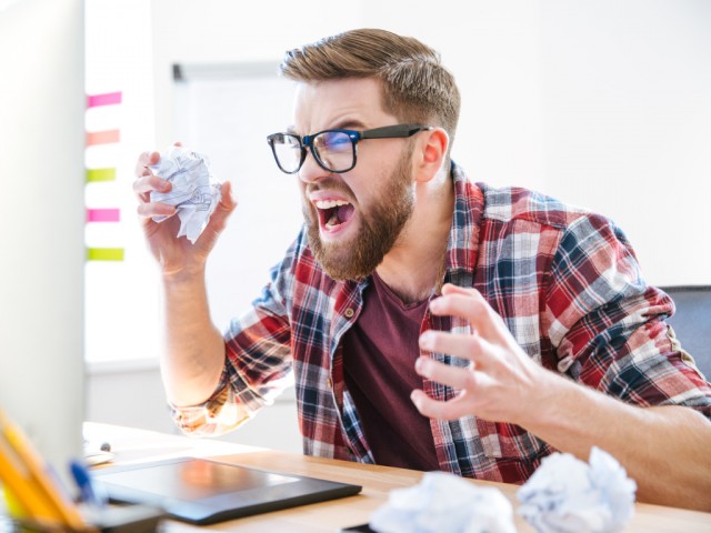 Angry crazy designer yelling and crumpling paper on his workplace