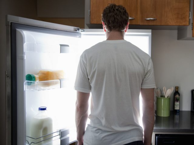 Man standing looking at contents of fridge