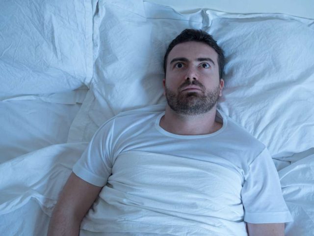 Thoughtful man trying to sleep in his bed at night